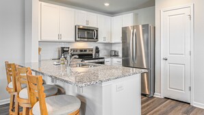 A modern kitchen with white cabinets, stainless steel appliances, a granite countertop, and wooden bar stools. - 3 Mi to Shore: Family Townhome in Surfside Beach (Surfside Beach)