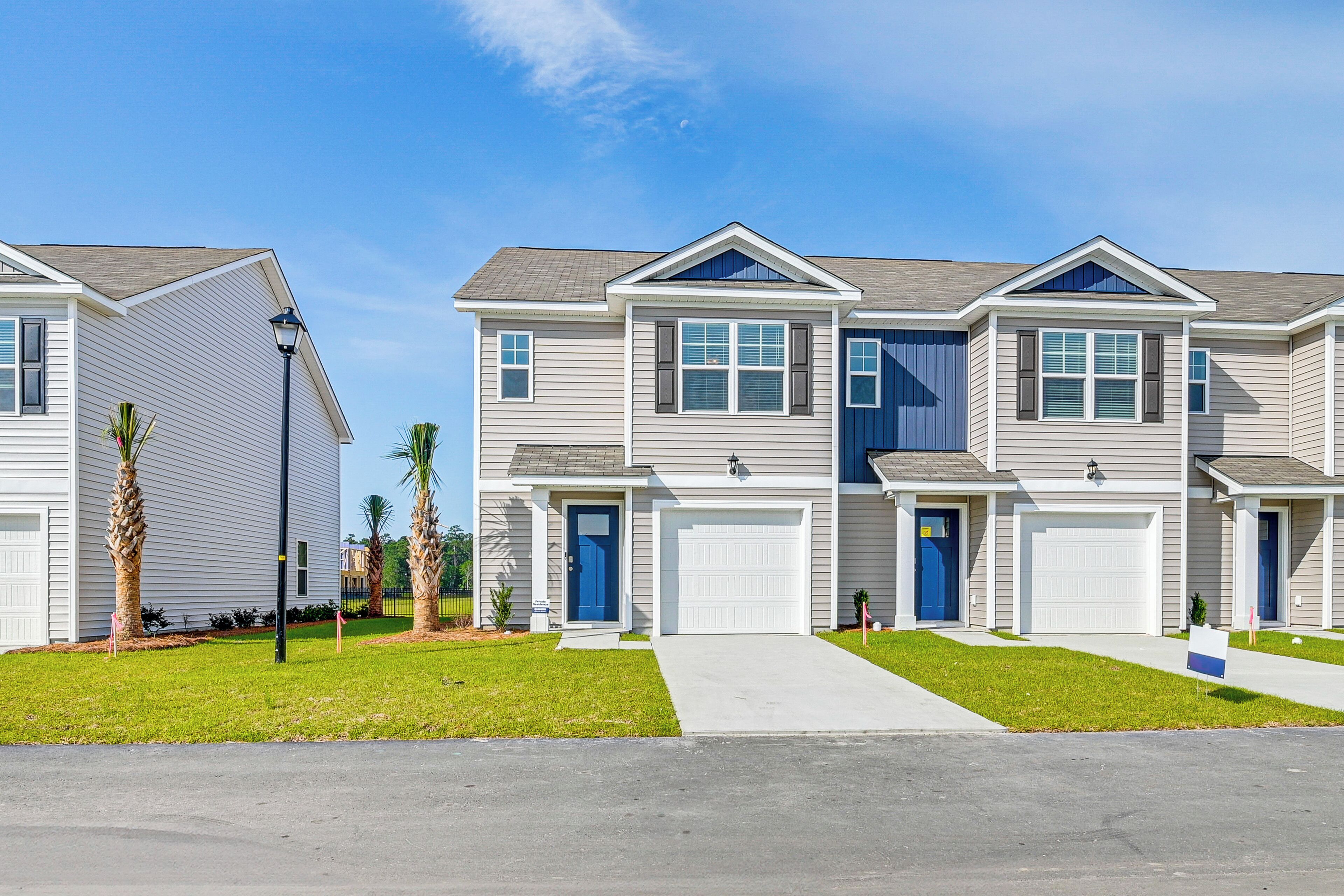 A row of townhouses with front garages, a clear sky, and a well-maintained lawn.