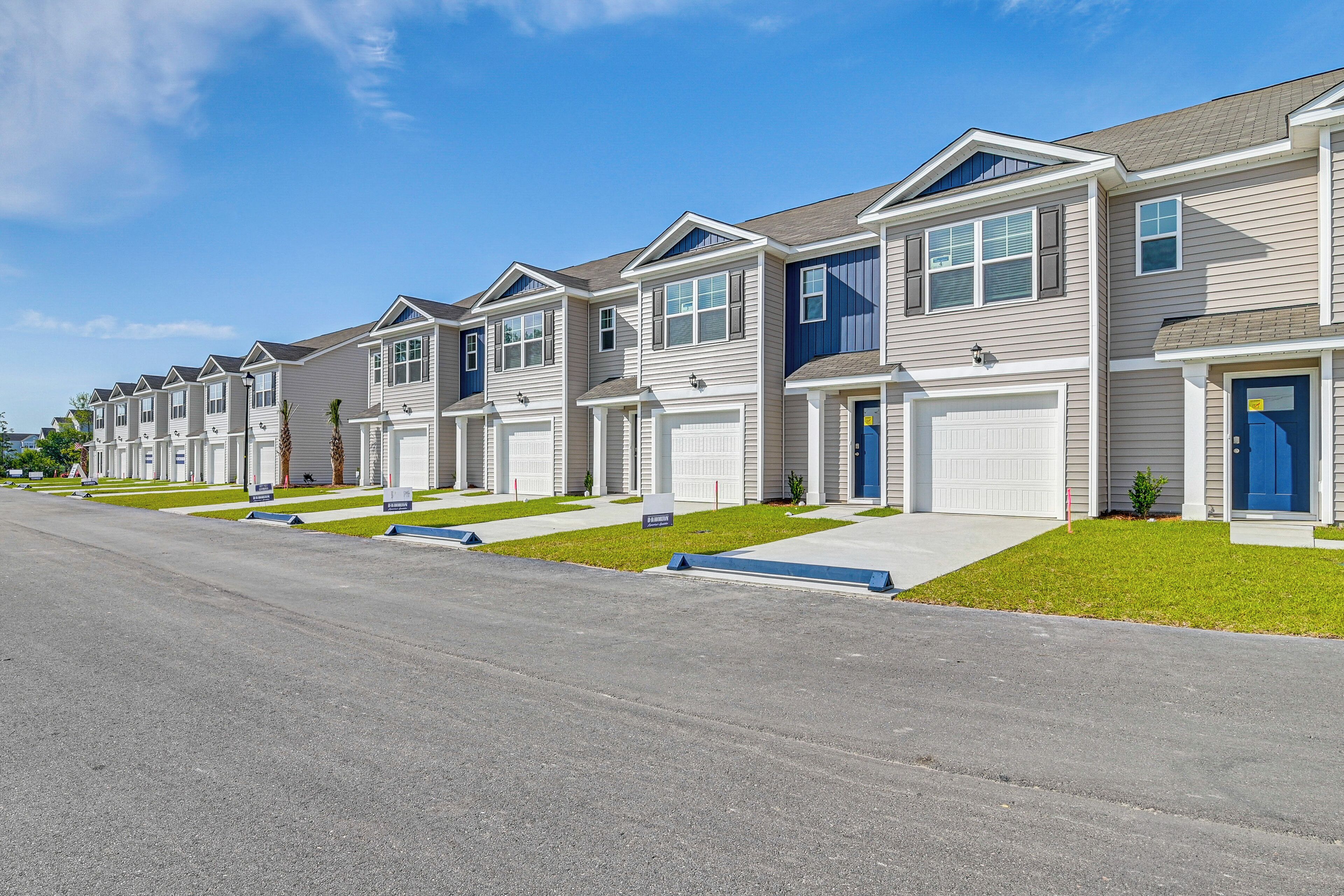 A row of townhouses with individual garages, neatly aligned on a street with a clear sky.