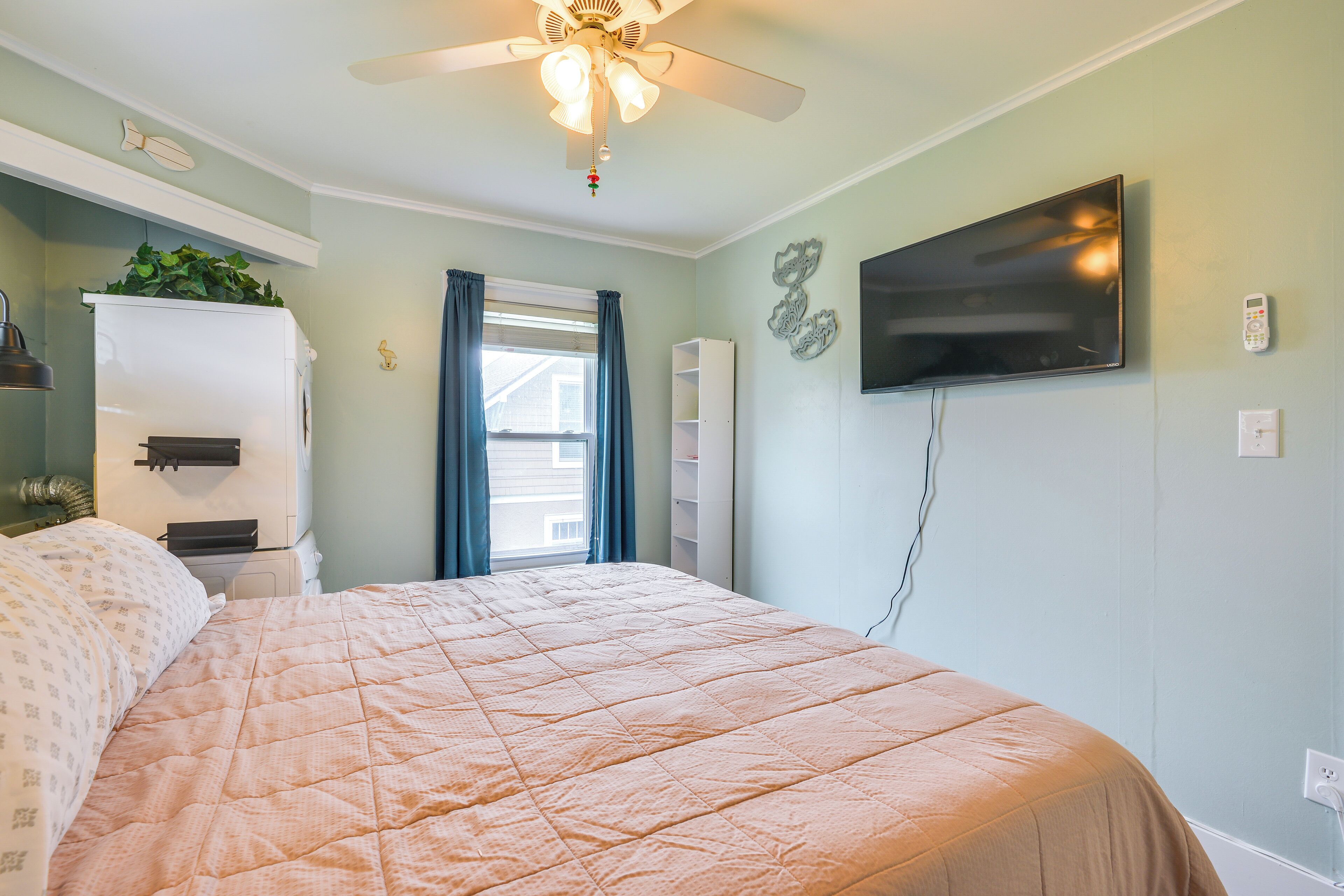 Une chambre à coucher avec un lit, un ventilateur de plafond, une télévision et une fenêtre avec des rideaux.