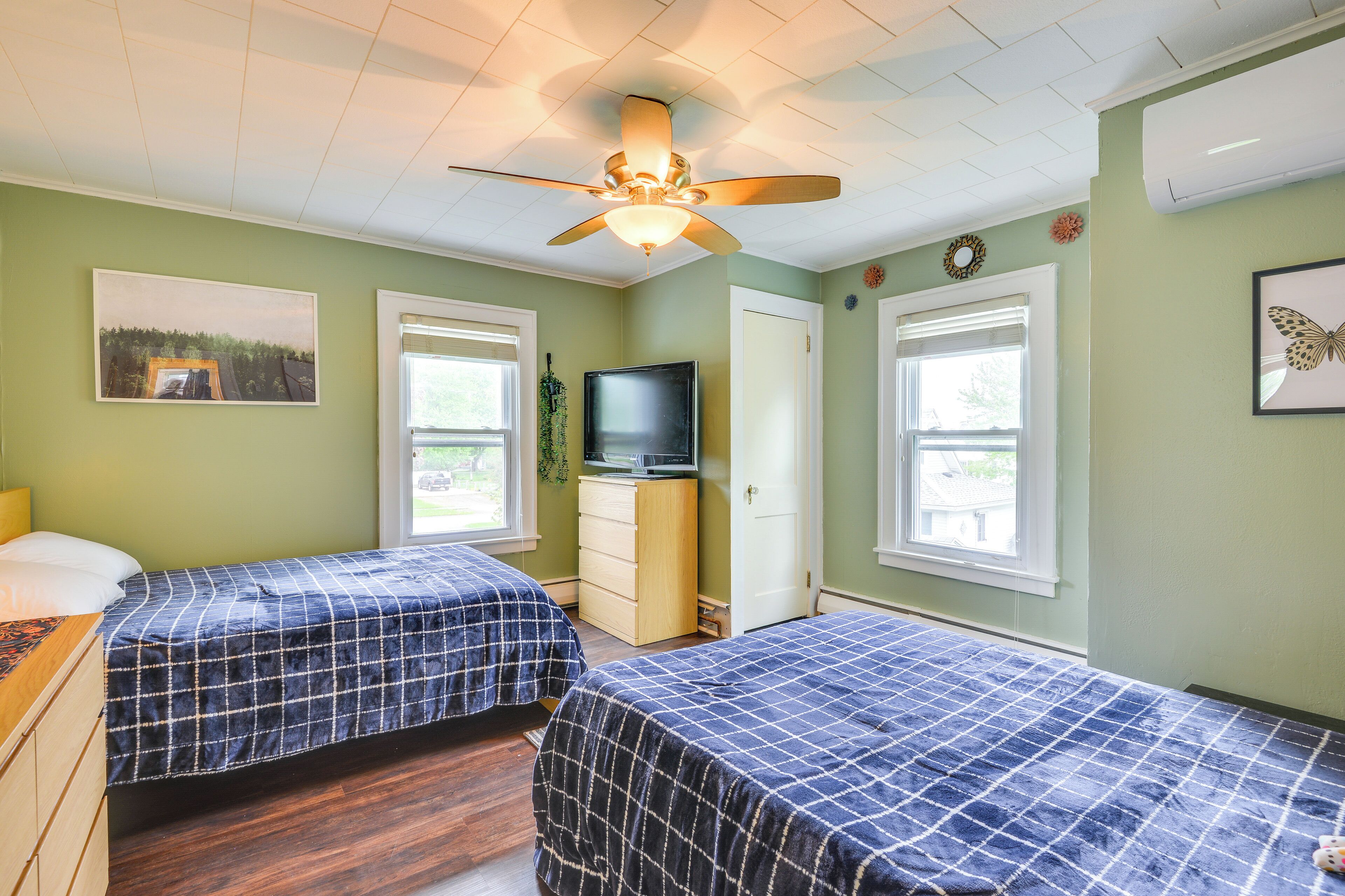 Ein Schlafzimmer mit zwei Betten, einem Deckenventilator, einem Fernseher und einem Fenster.