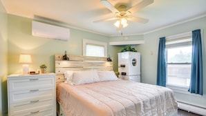 Un dormitorio con cama, mesita de noche, cómoda, ventilador de techo y ventana con cortinas.