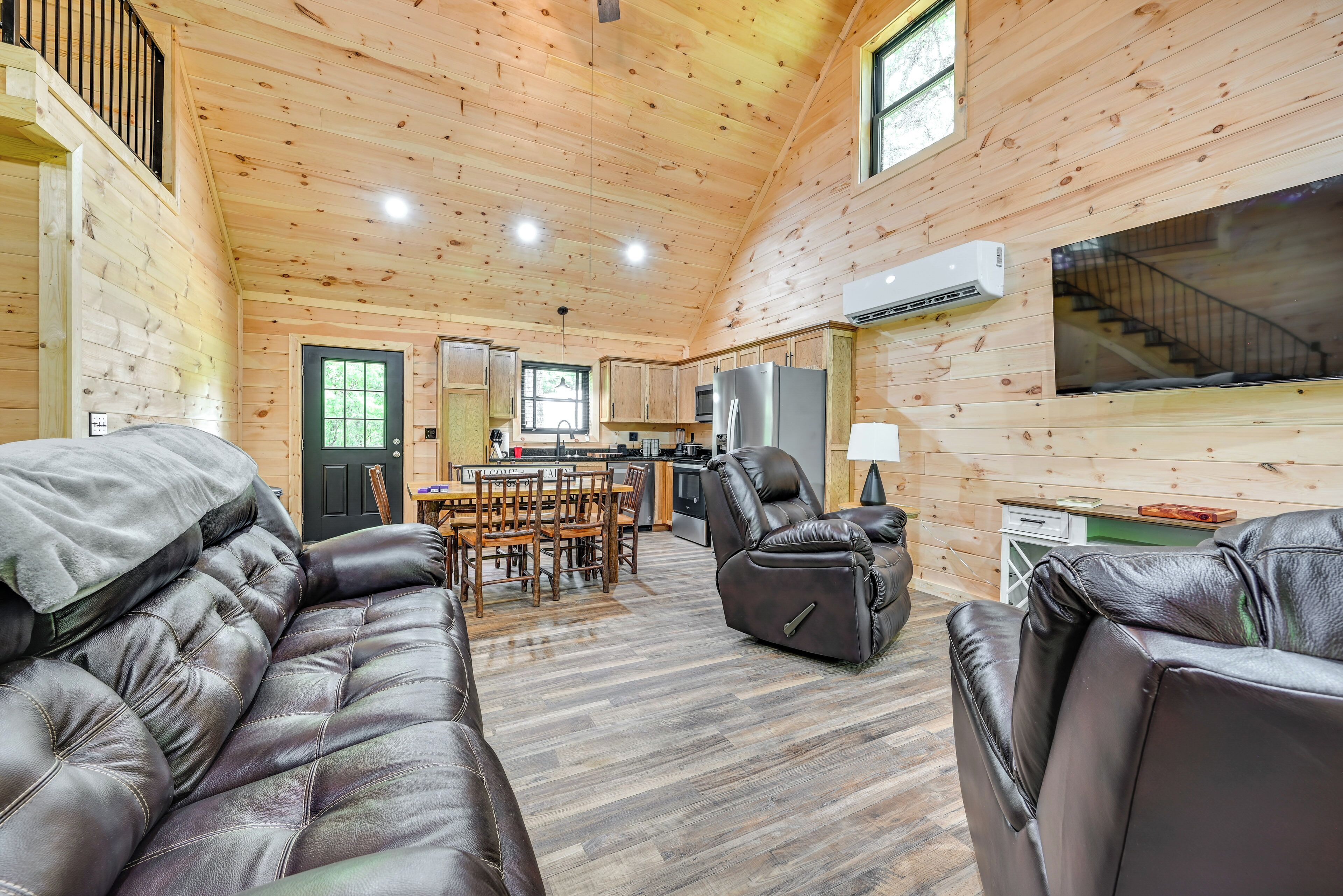 A log cabin interior with a dining area, kitchen, and a leather sofa.