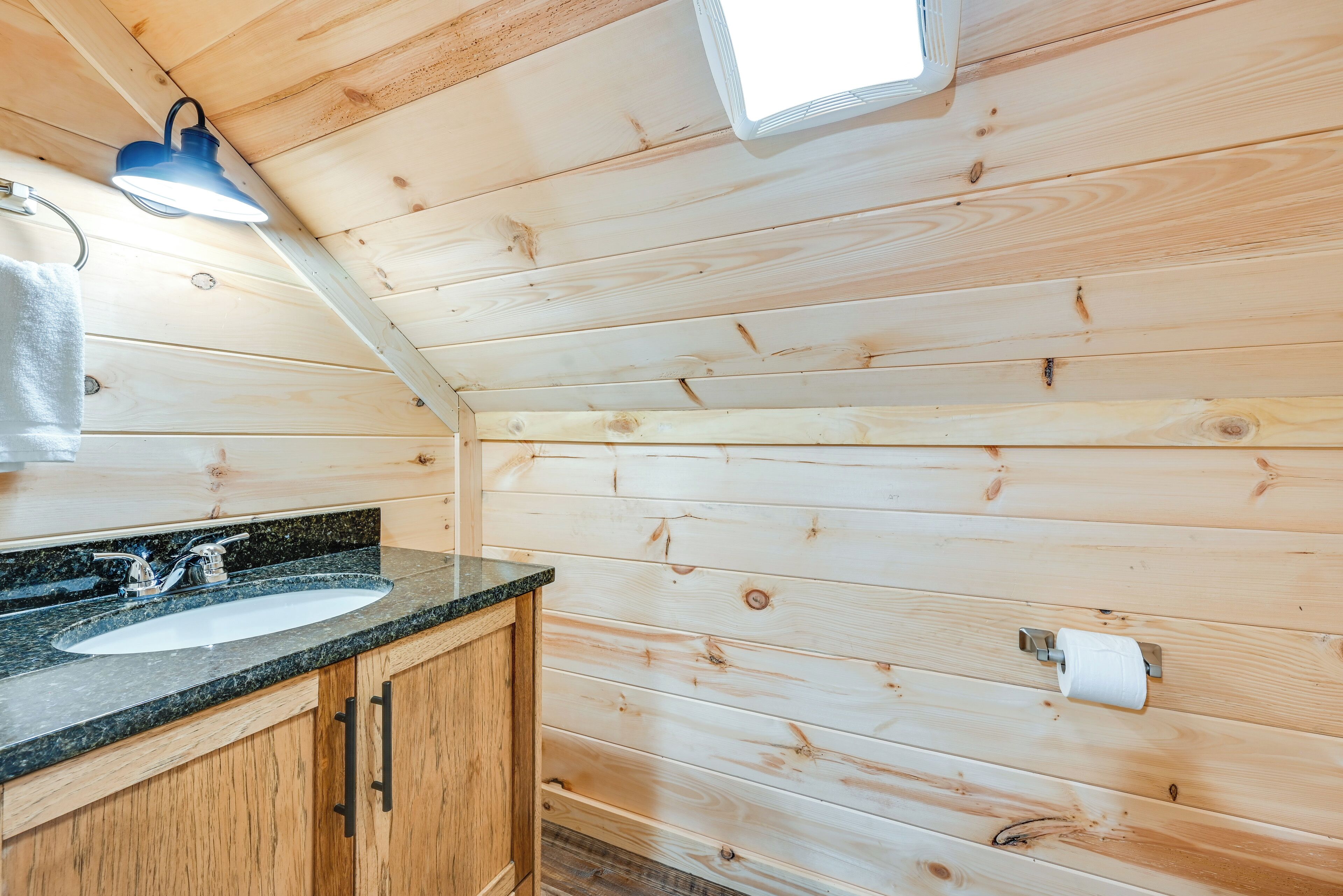 A wooden cabin bathroom with a granite countertop sink, wooden cabinets, a towel hanging on the wall, and a ceiling light fixture.