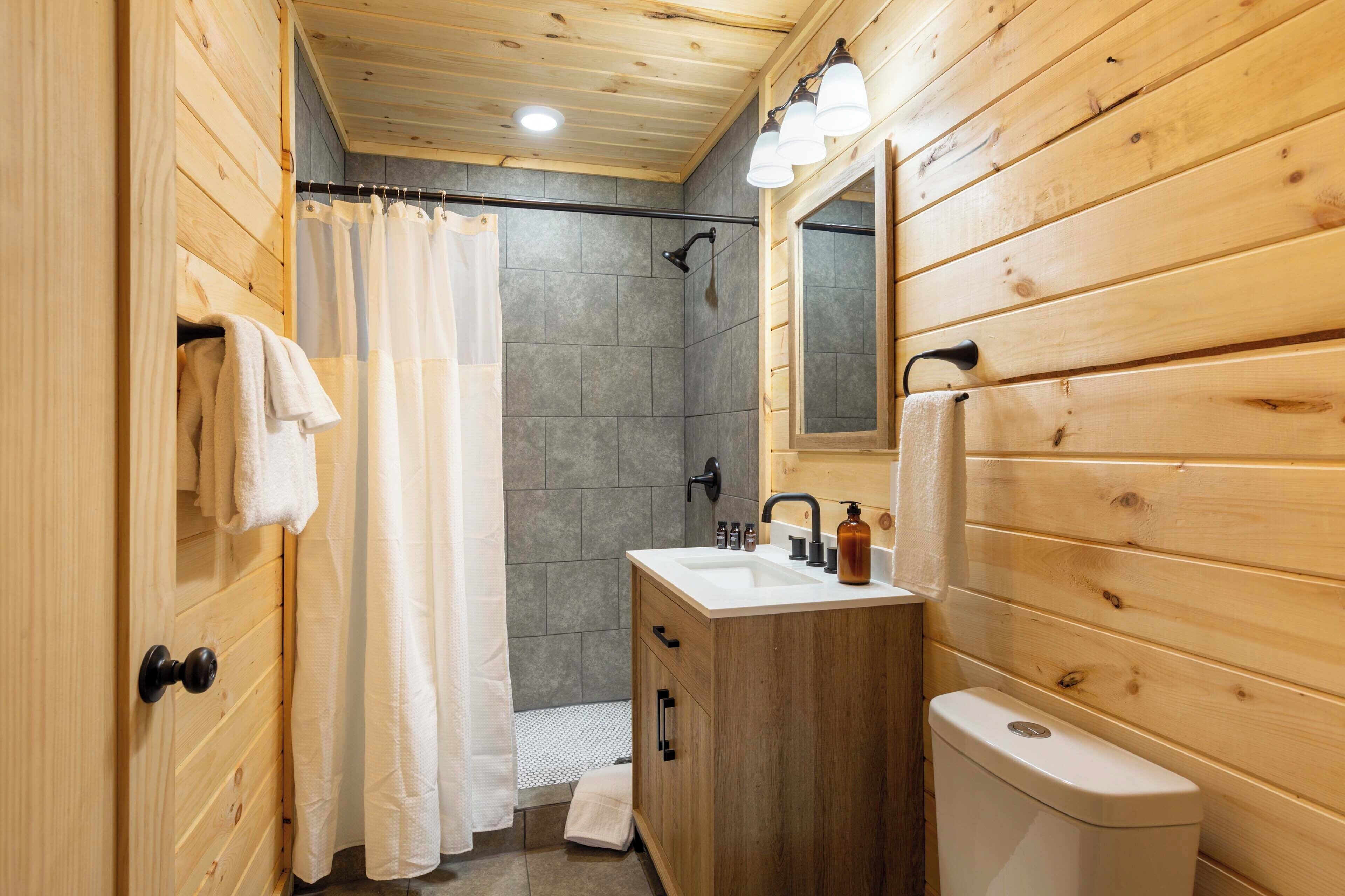 A wooden-paneled bathroom with a shower, sink, and toilet.