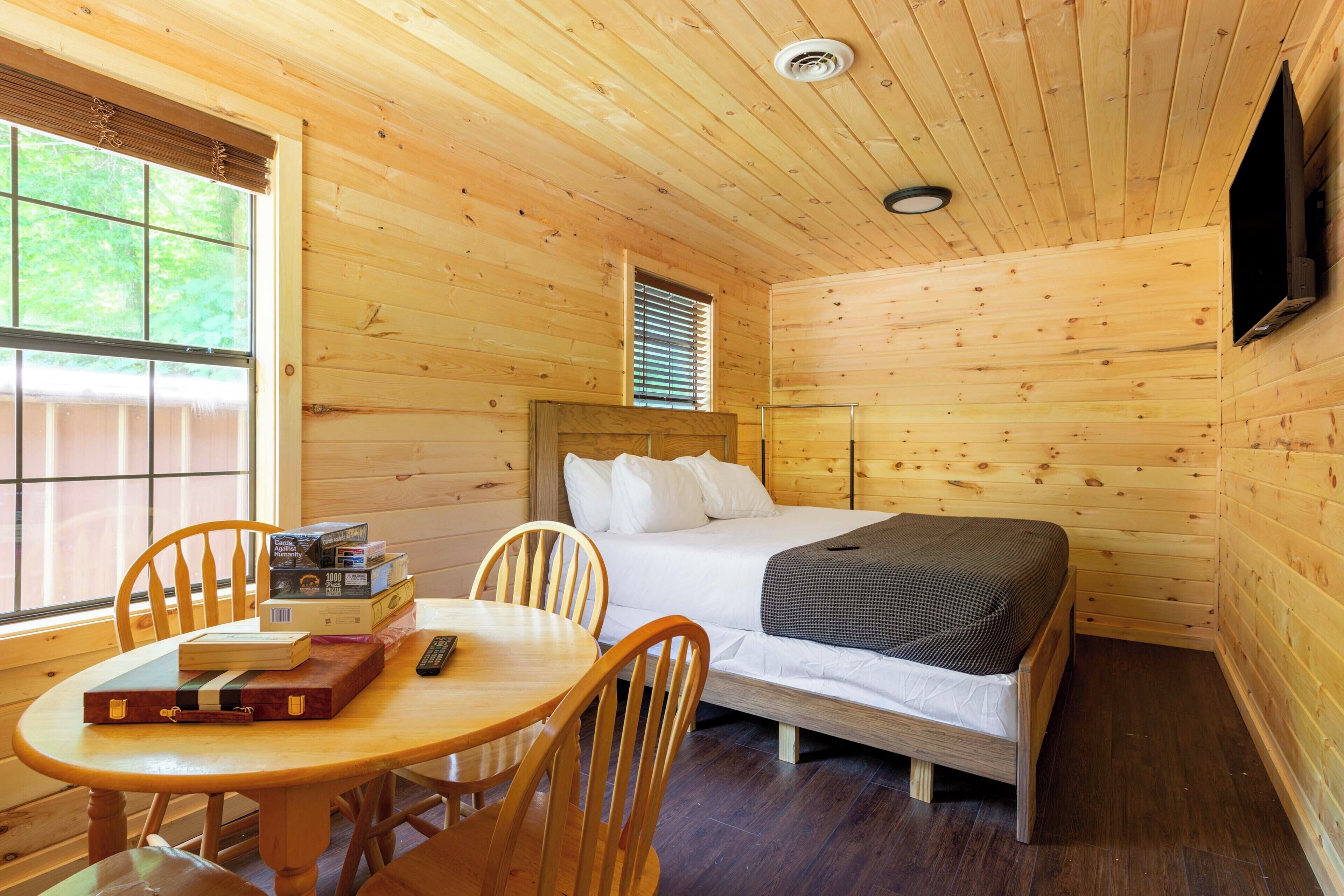 Una habitación de cabaña de madera con una cama, una mesa y sillas, y una ventana.