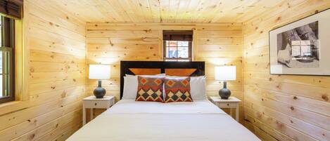 Une chambre à coucher dans un chalet en bois, avec un lit, deux tables de chevet, deux lampes et un tableau encadré au mur.