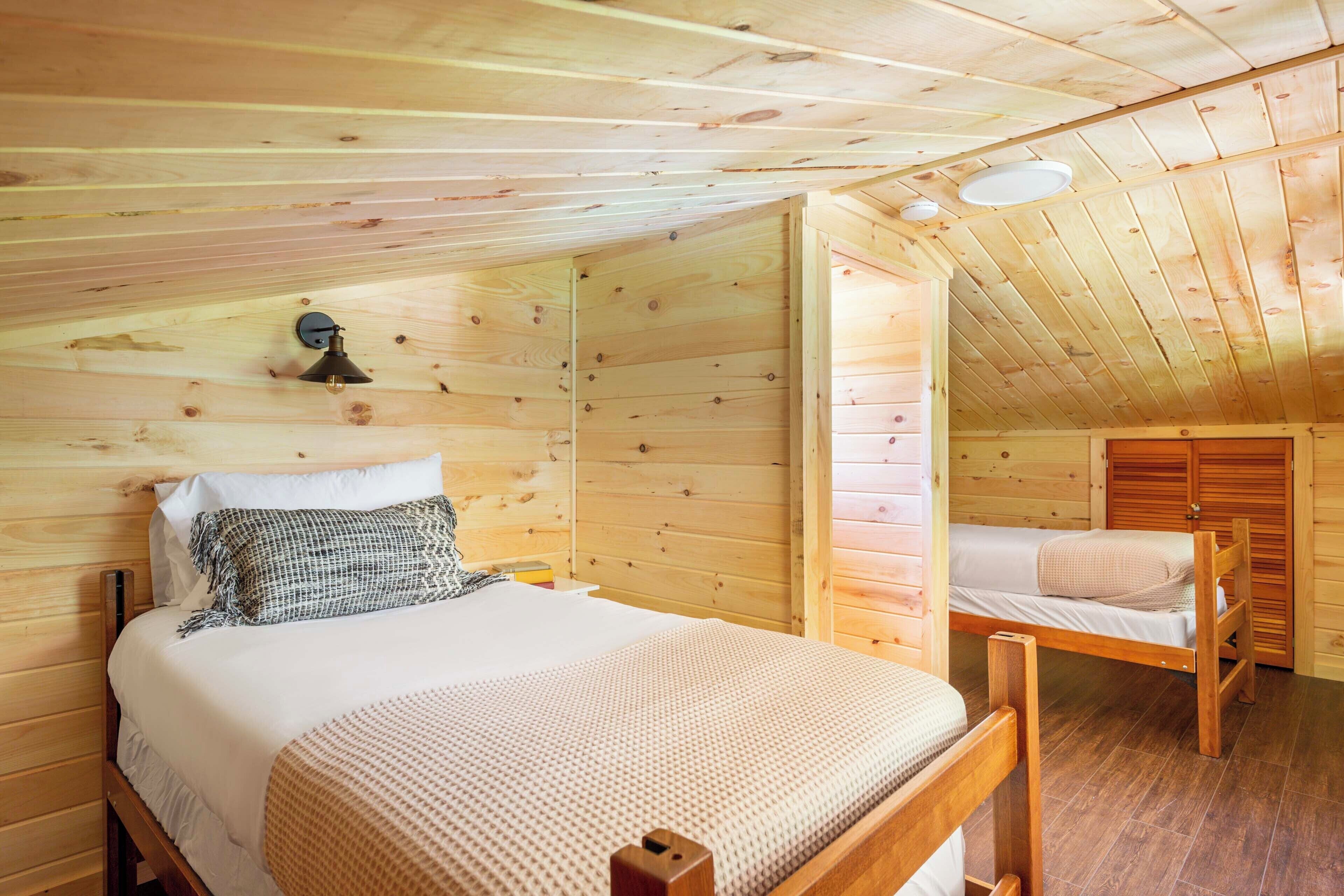 A wooden cabin bedroom with a bed, a smaller bed, and a nightstand.