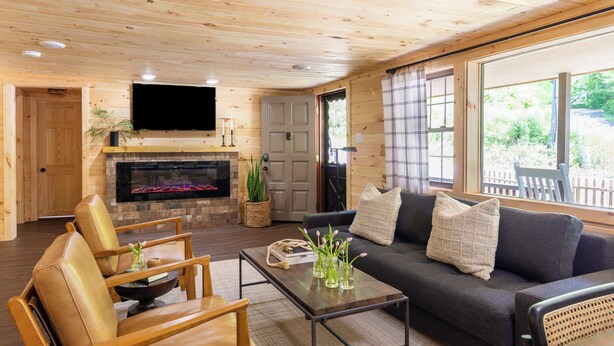 A cozy living room with a fireplace, leather chairs, a sofa, and large windows offering a view of the outdoors. - 2 Mi to Dtwn: Spacious Gatlinburg Home w/ Hot Tub! (Gatlinburg)