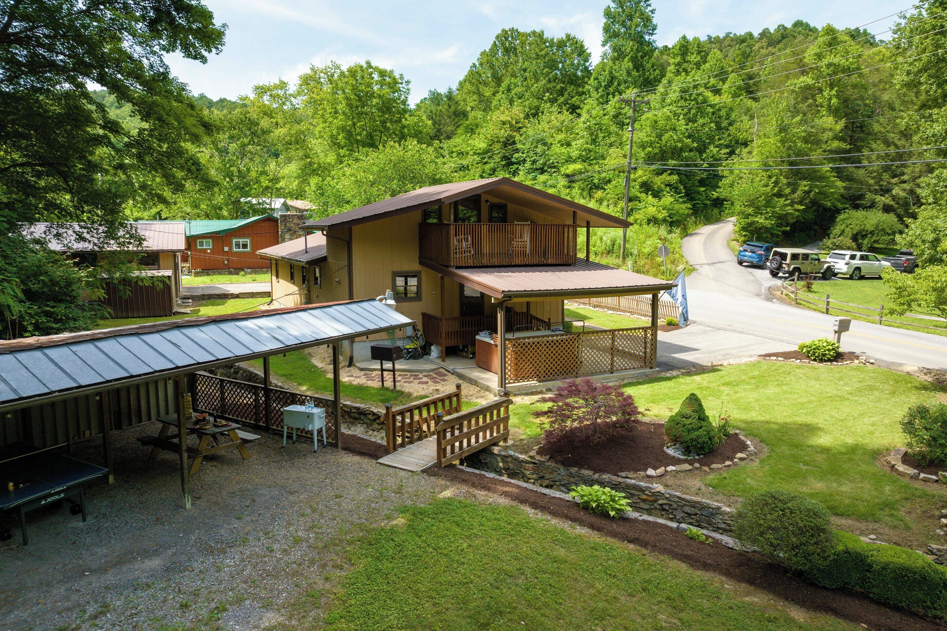 Eine zweistöckige Lodge mit überdachter Veranda, einer kleinen Terrasse und einem eingezäunten Garten mit Picknicktisch und Grill.
