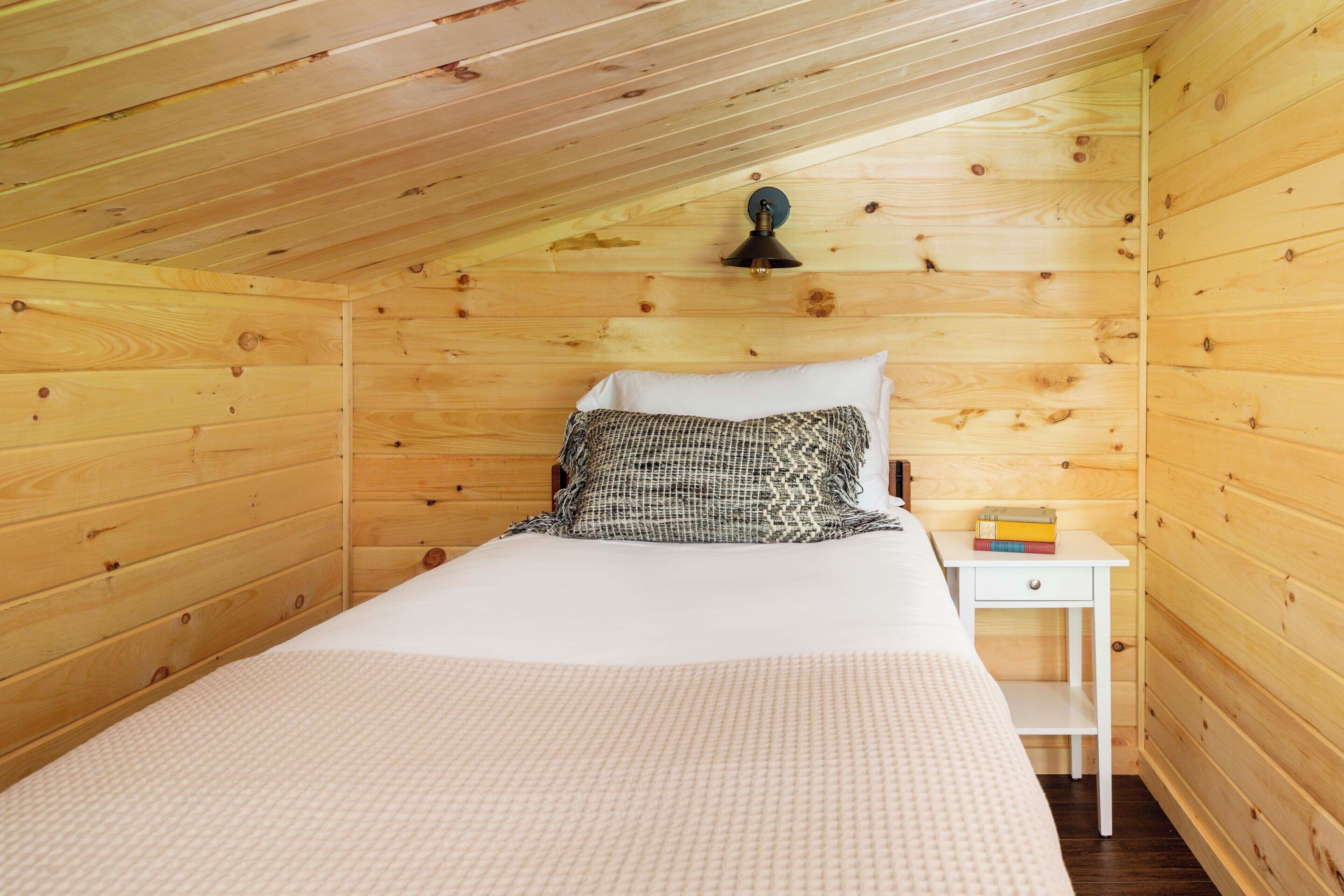 A cozy wooden room with a bed, a nightstand, and a lamp.