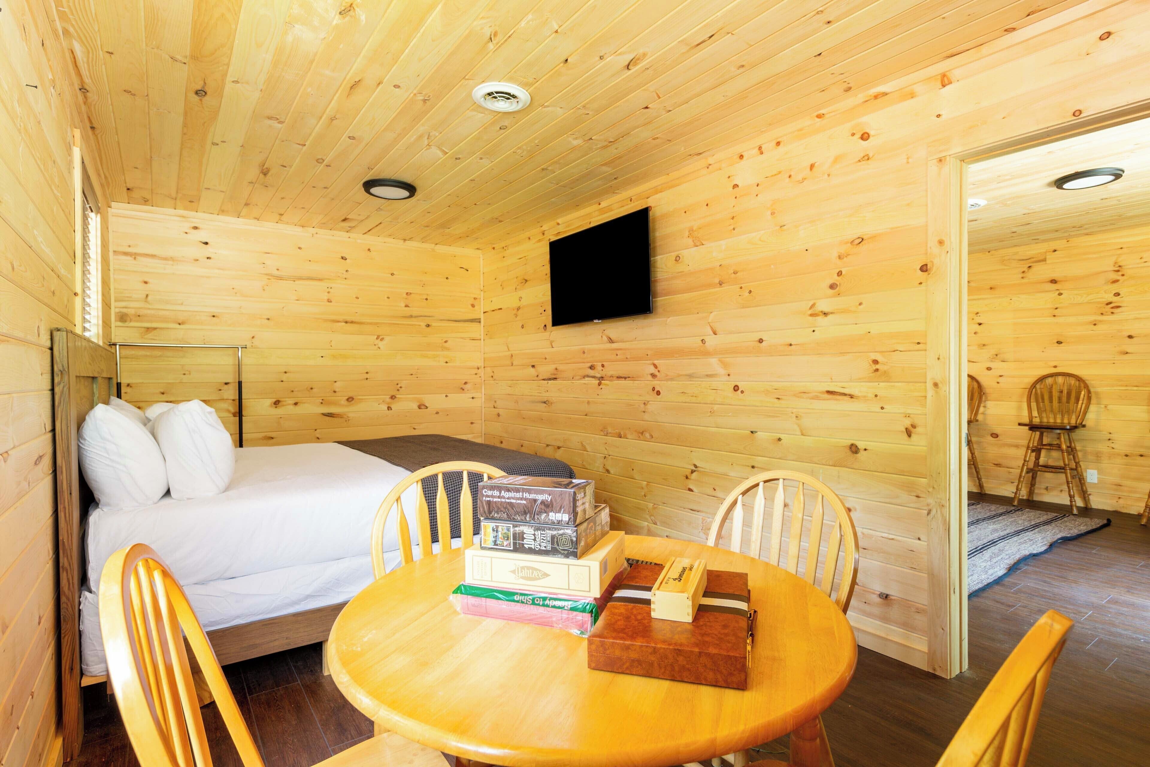 Ein Holzhütten-Zimmer mit einem Bett, einem Tisch mit Büchern und einem an der Wand befestigten Fernseher.
