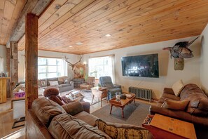 A cozy living room with a large wooden ceiling, leather sofas, a mounted deer head, and a television.