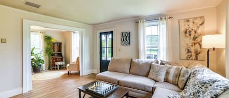 A living room with a beige sofa, a coffee table with a chess set, a lamp, and a painting on the wall.