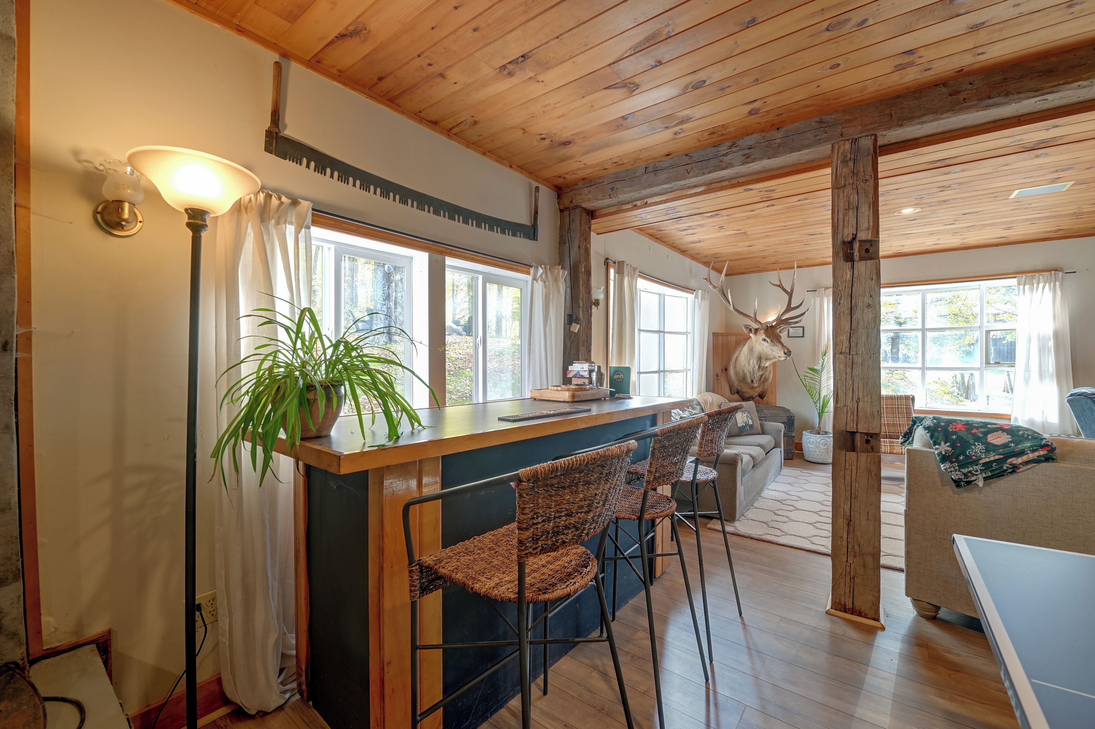 A rustic interior with a wooden ceiling, a bar area with woven chairs, and a large antler decoration.