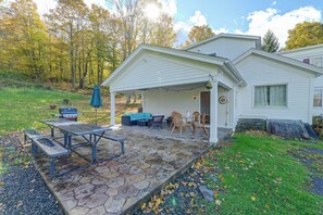 A house with a covered patio, stone flooring, outdoor furniture, and a barbecue grill.