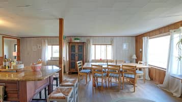 A dining area with a wooden table and chairs, a kitchen counter with a bowl, and a window with curtains.