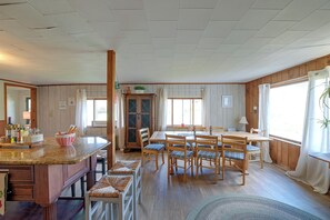 A dining area with a wooden table and chairs, a kitchen counter with a bowl, and a window with curtains.