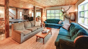 A cozy living room with a wooden ceiling, a mounted deer head, and a large window.