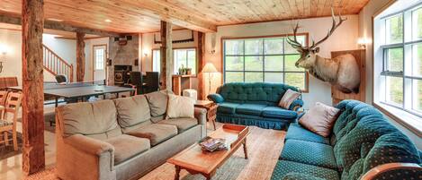 A cozy living room with a wooden ceiling, a mounted deer head, and a large window.