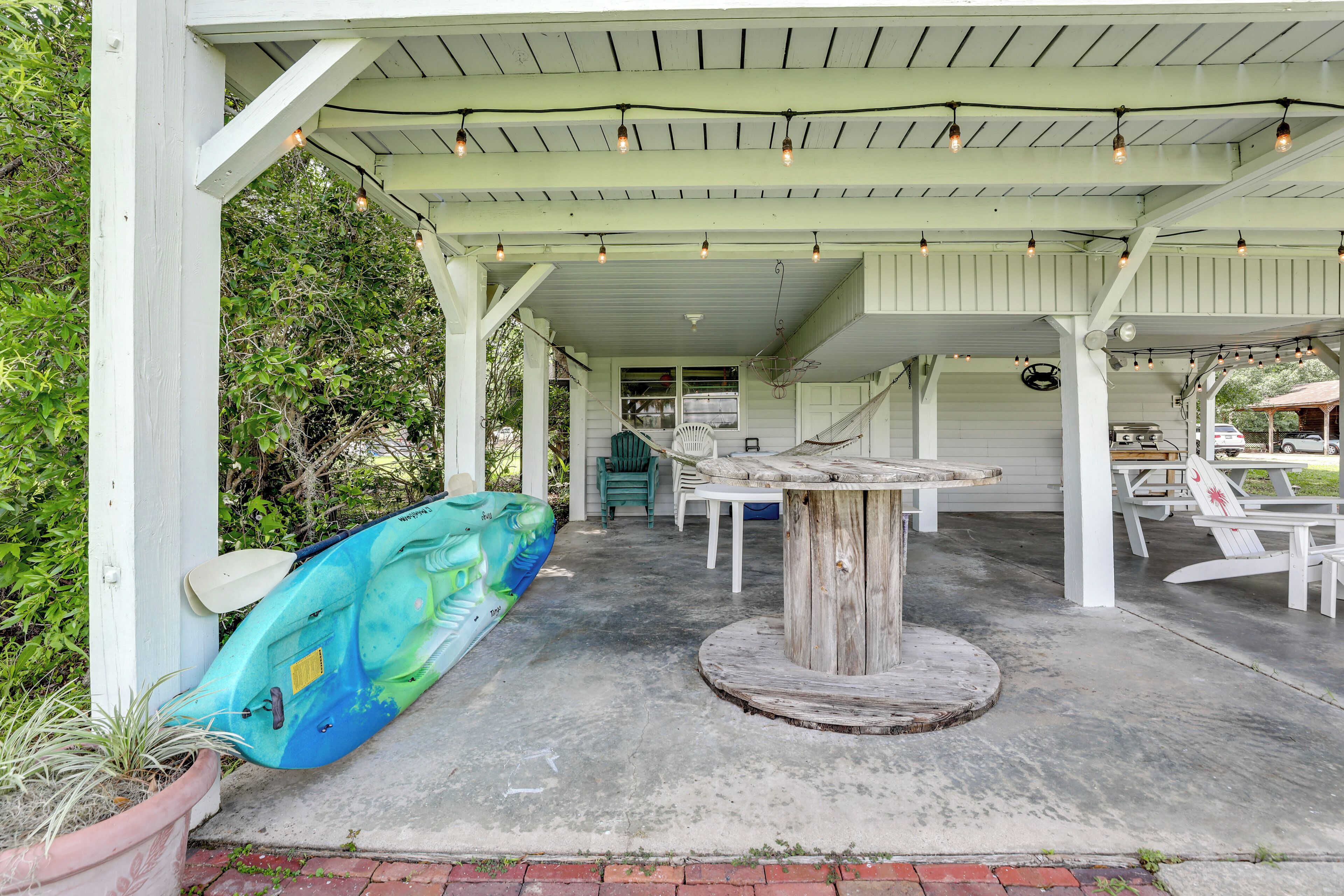A covered outdoor area with a concrete floor, a wooden table, and a kayak leaning against a white post.