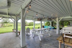 A covered outdoor area with picnic tables and chairs, a grill, and a view of a swimming pool and greenery. - Spacious Riverfront Cottage w/ Dock in Green Pond! (Jacksonboro)