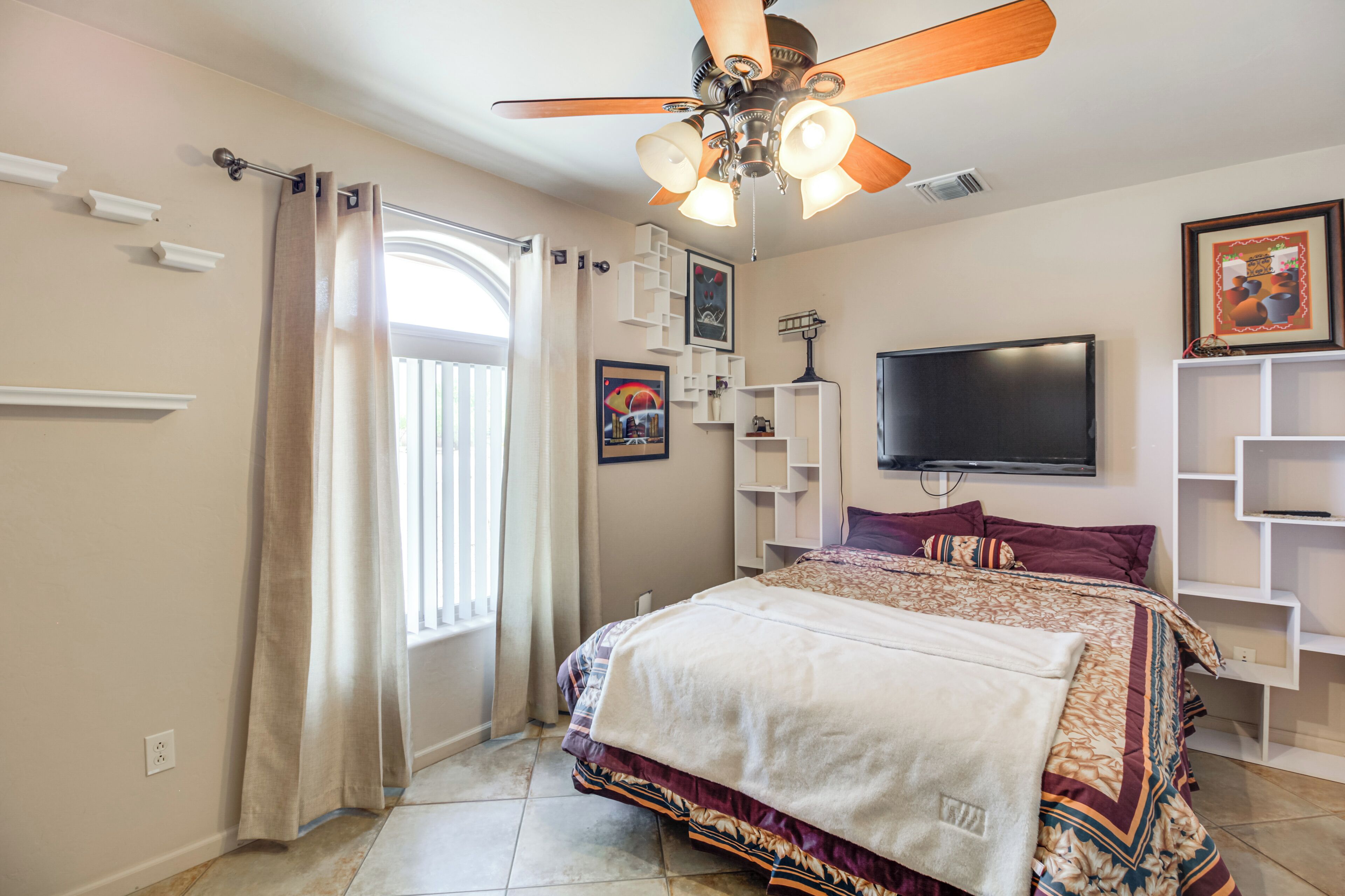 A bedroom with a bed, a ceiling fan, a TV, and built-in shelving.