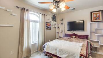 A bedroom with a bed, a ceiling fan, a TV, and built-in shelving.