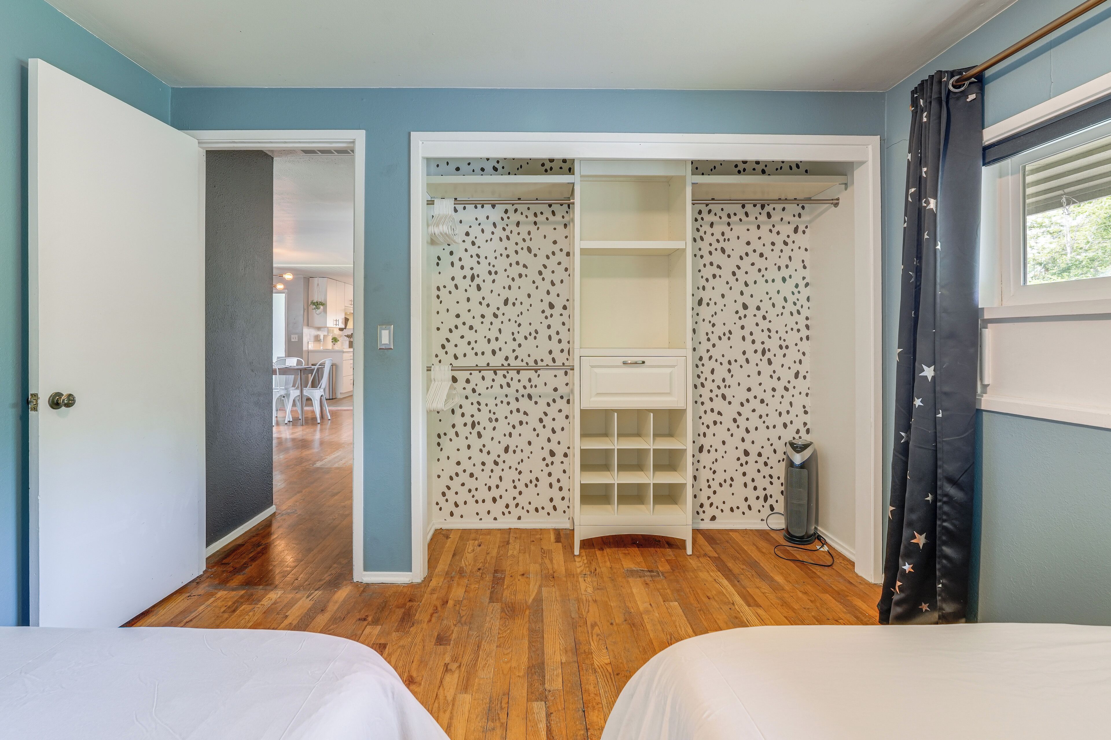 Ein Schlafzimmer mit zwei Betten, einem begehbaren Kleiderschrank mit gemusterten Vorhängen und einem Fenster mit Vorhang.