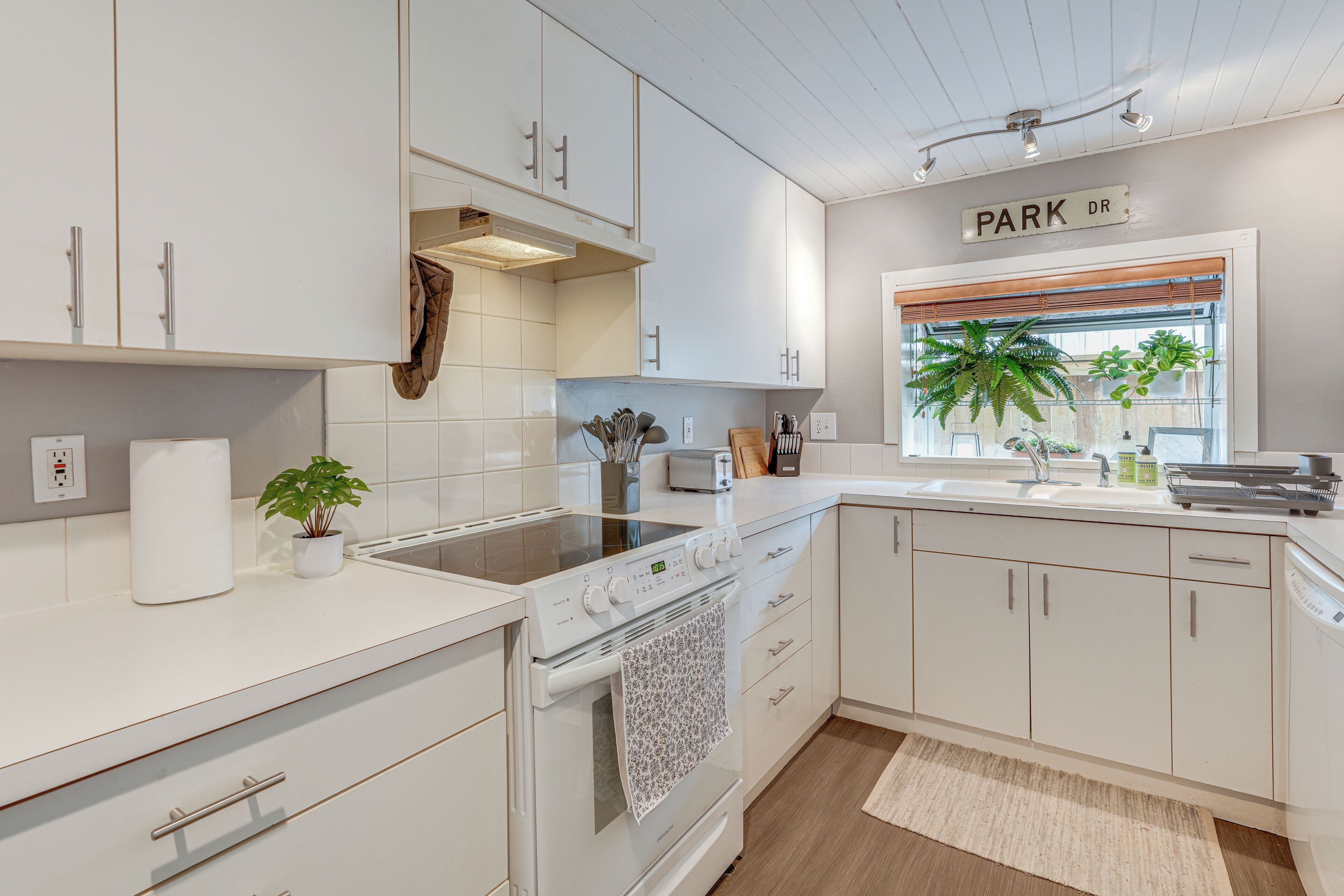 A modern kitchen with white cabinetry, a built-in oven, a stovetop, and a window with plants.