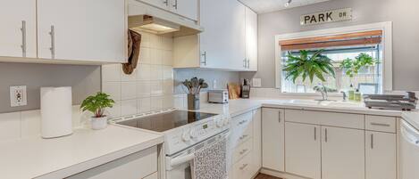 A modern kitchen with white cabinetry, a built-in oven, a stovetop, and a window with plants.
