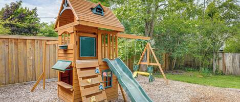 A wooden playhouse with a slide and climbing steps.