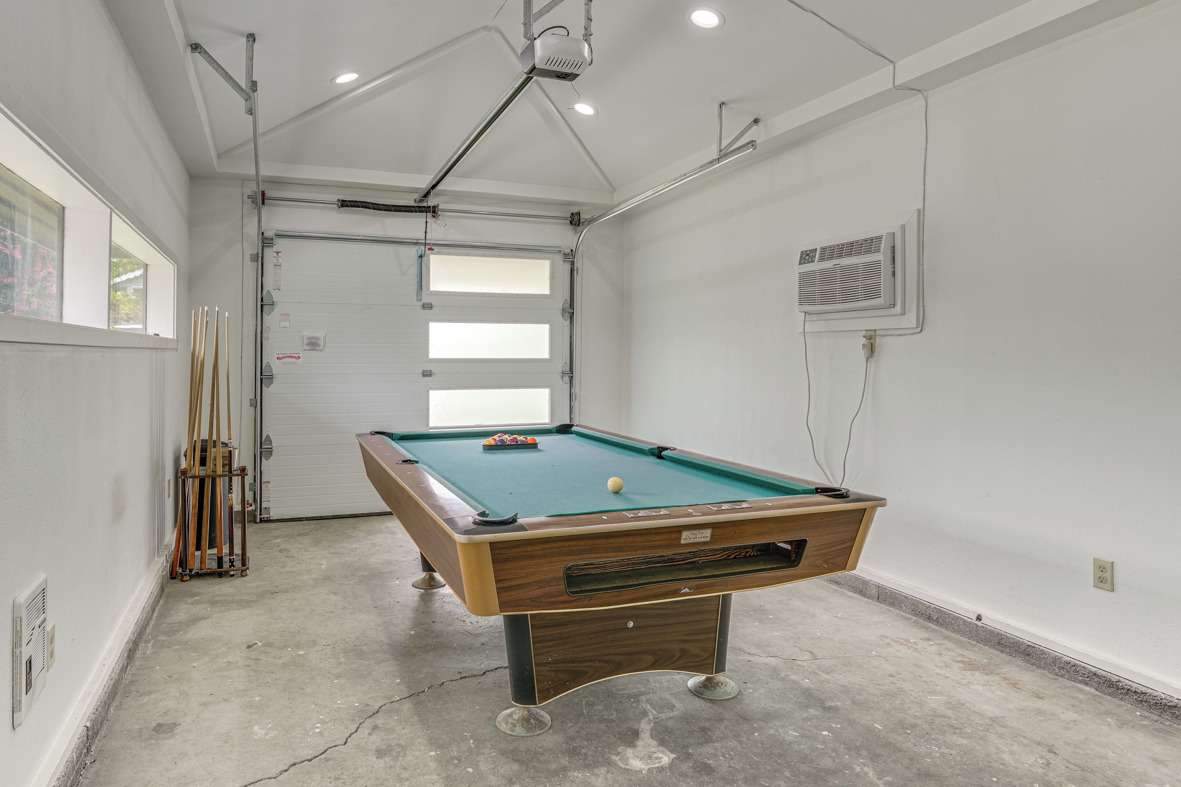 A pool table in a room with a concrete floor, a window, and a door.