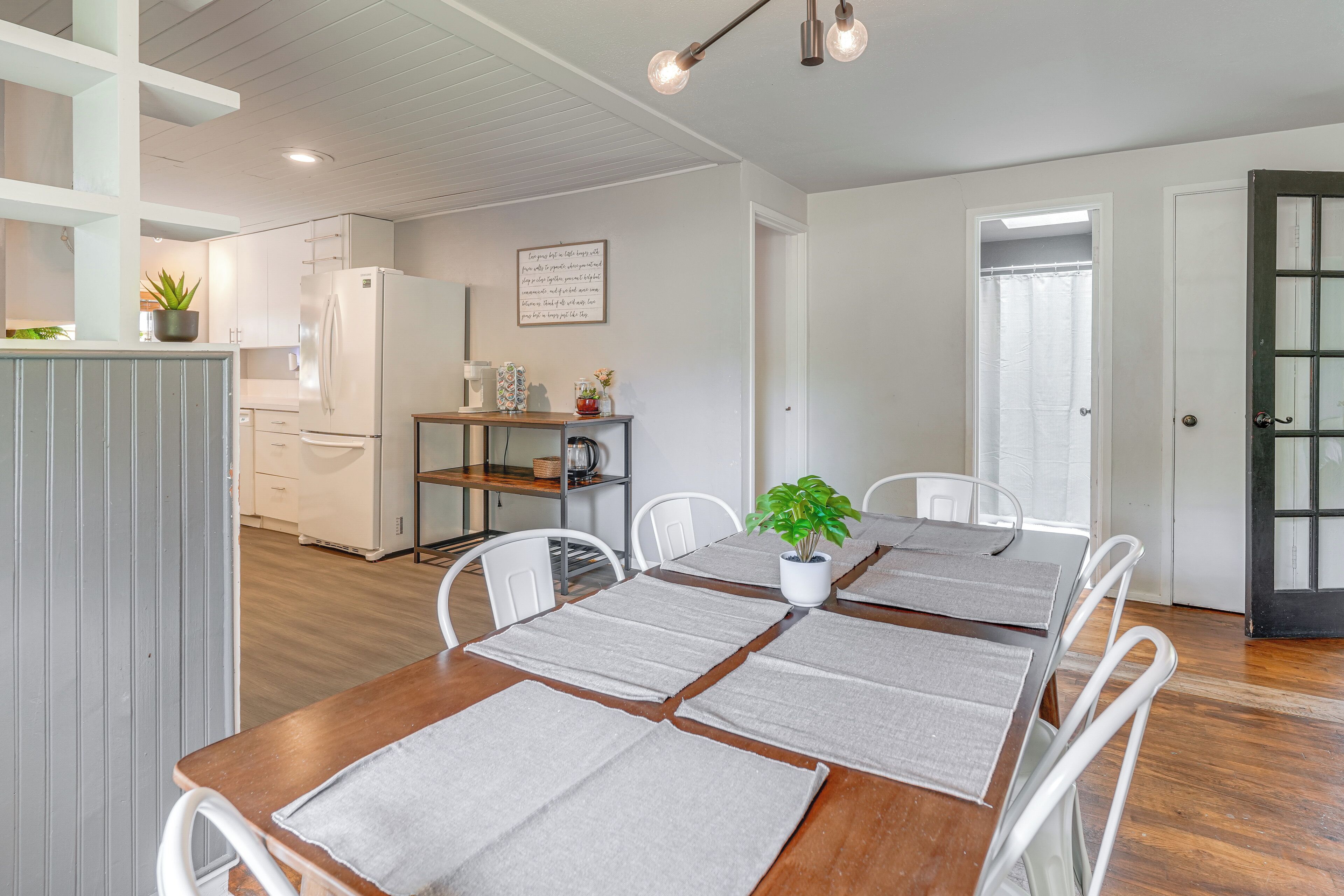 A dining area with a wooden table set for four, white chairs, and a potted plant on the table.