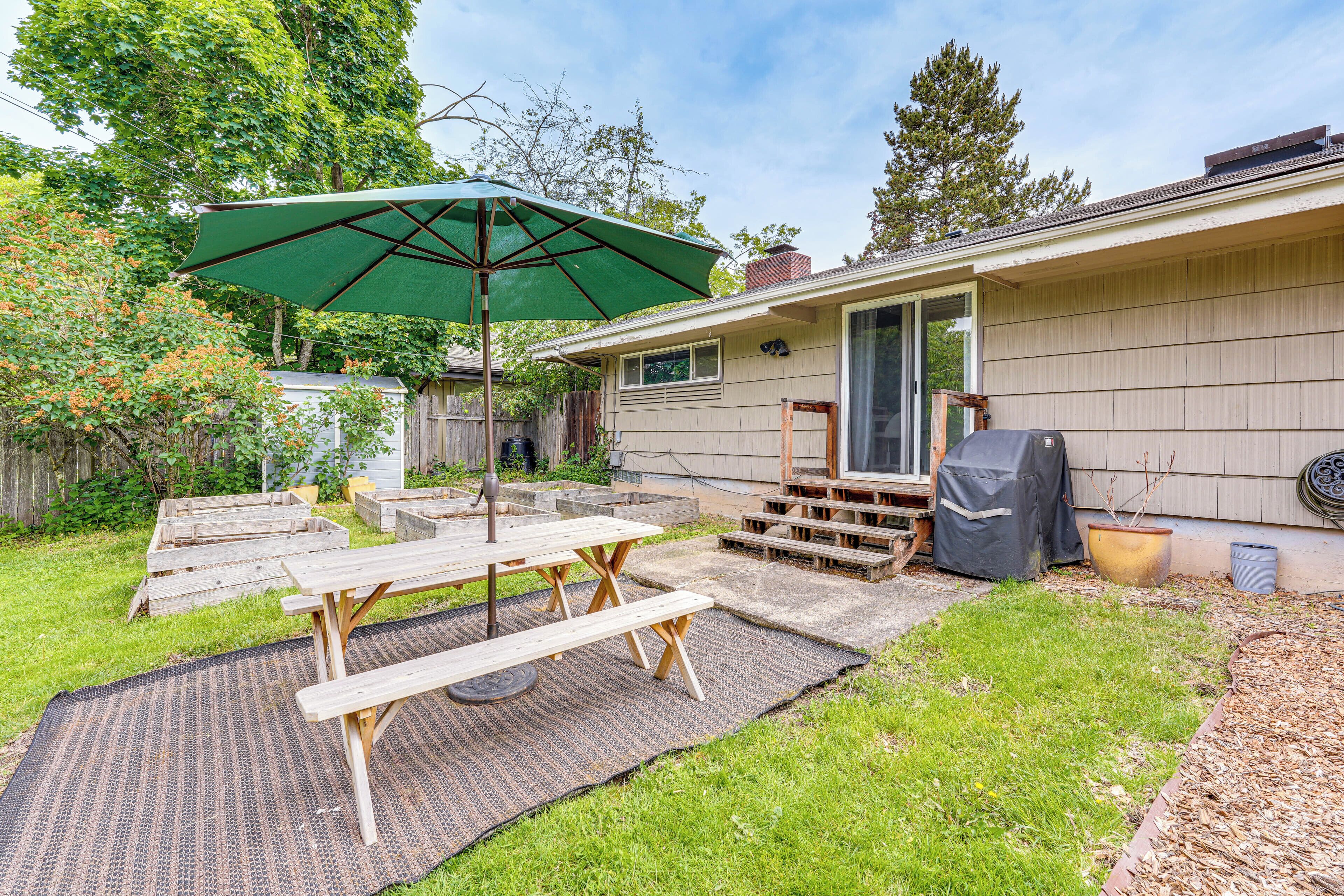 Un patio trasero con una mesa de picnic, una sombrilla verde y una parrilla de barbacoa.
