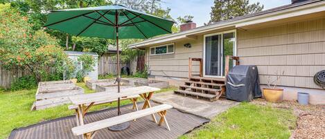 Un patio trasero con una mesa de picnic, una sombrilla verde y una parrilla de barbacoa.
