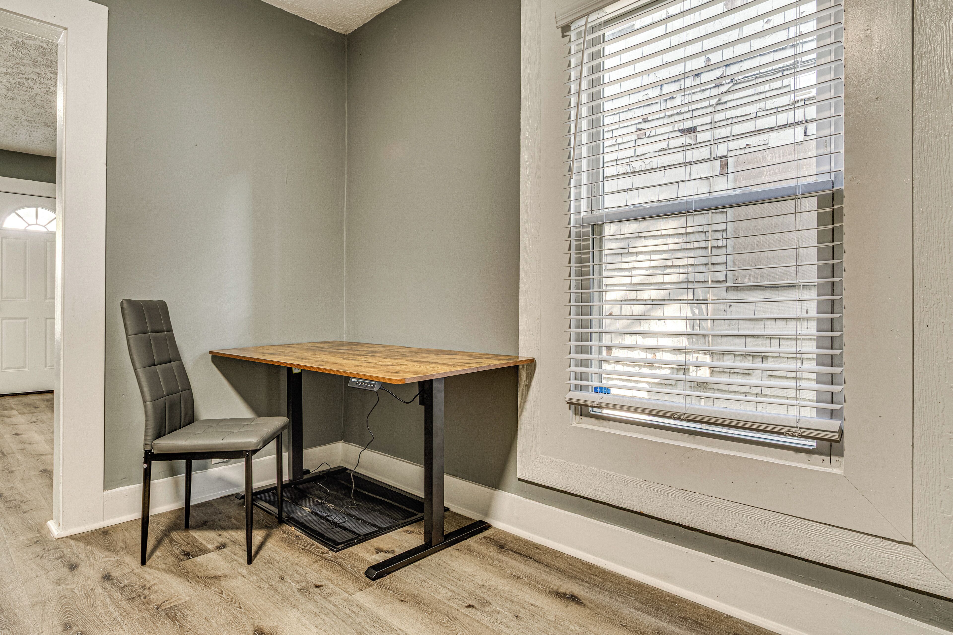 A corner room with a small table and chair, a window with blinds, and a door.