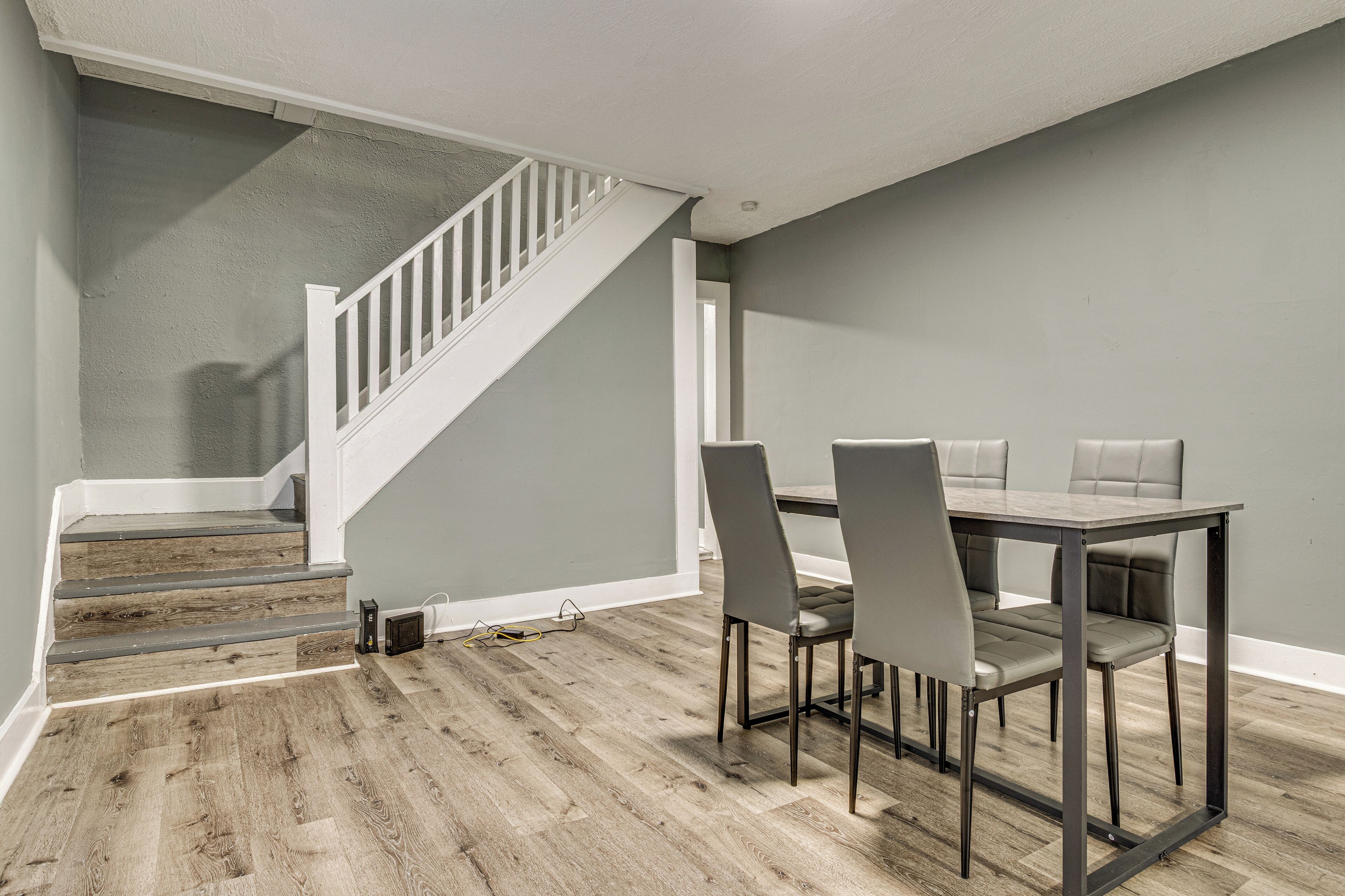 A dining area with a wooden staircase, grey walls, and a table with four chairs.