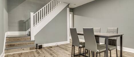 A dining area with a wooden staircase, grey walls, and a table with four chairs.
