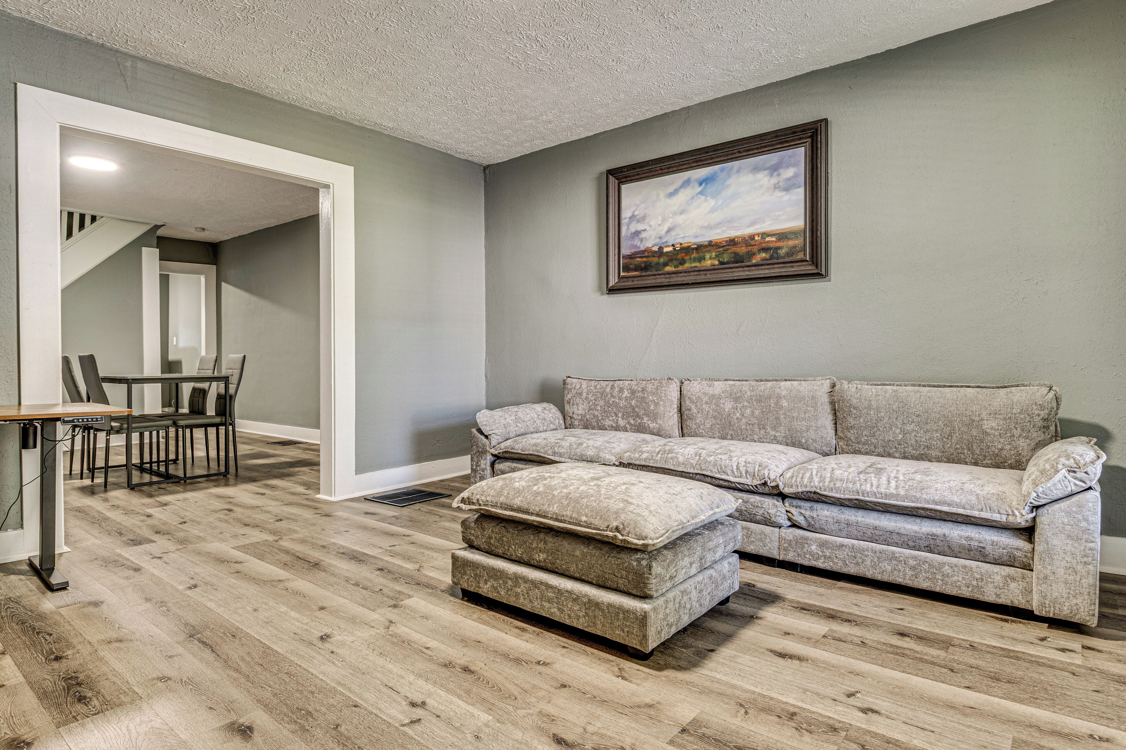 A living room with a grey couch, ottoman, and a painting on the wall.