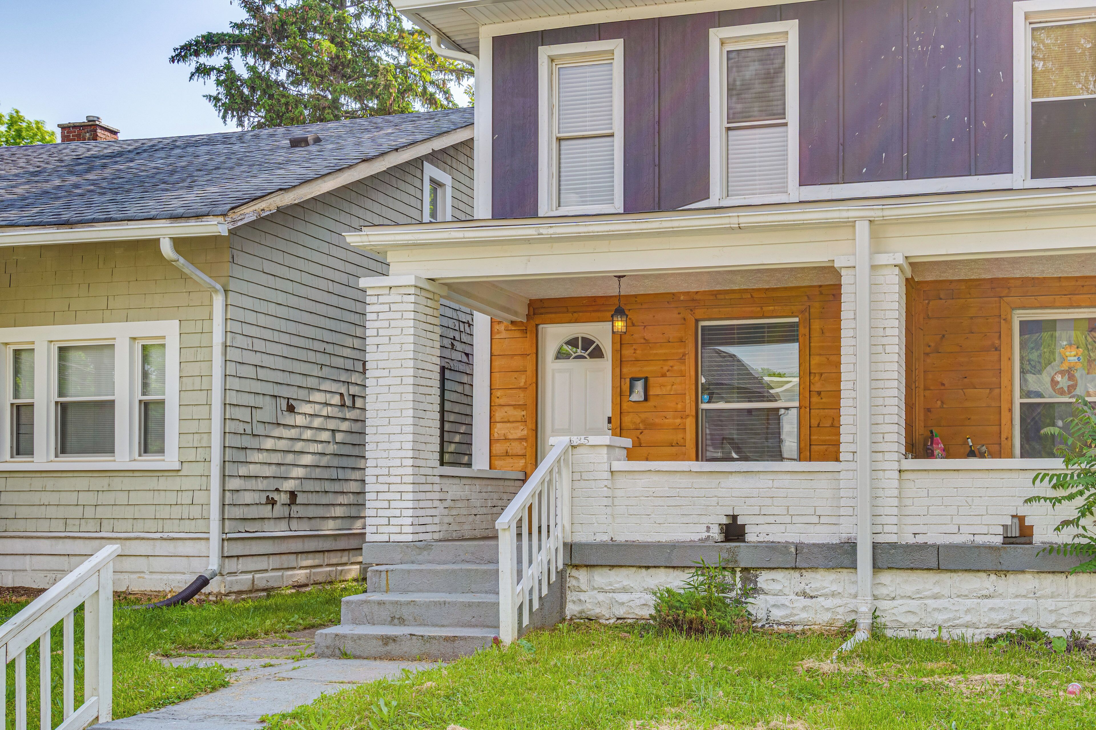 A two-story house with a front porch, a wooden door, and a small set of steps leading to the entrance.