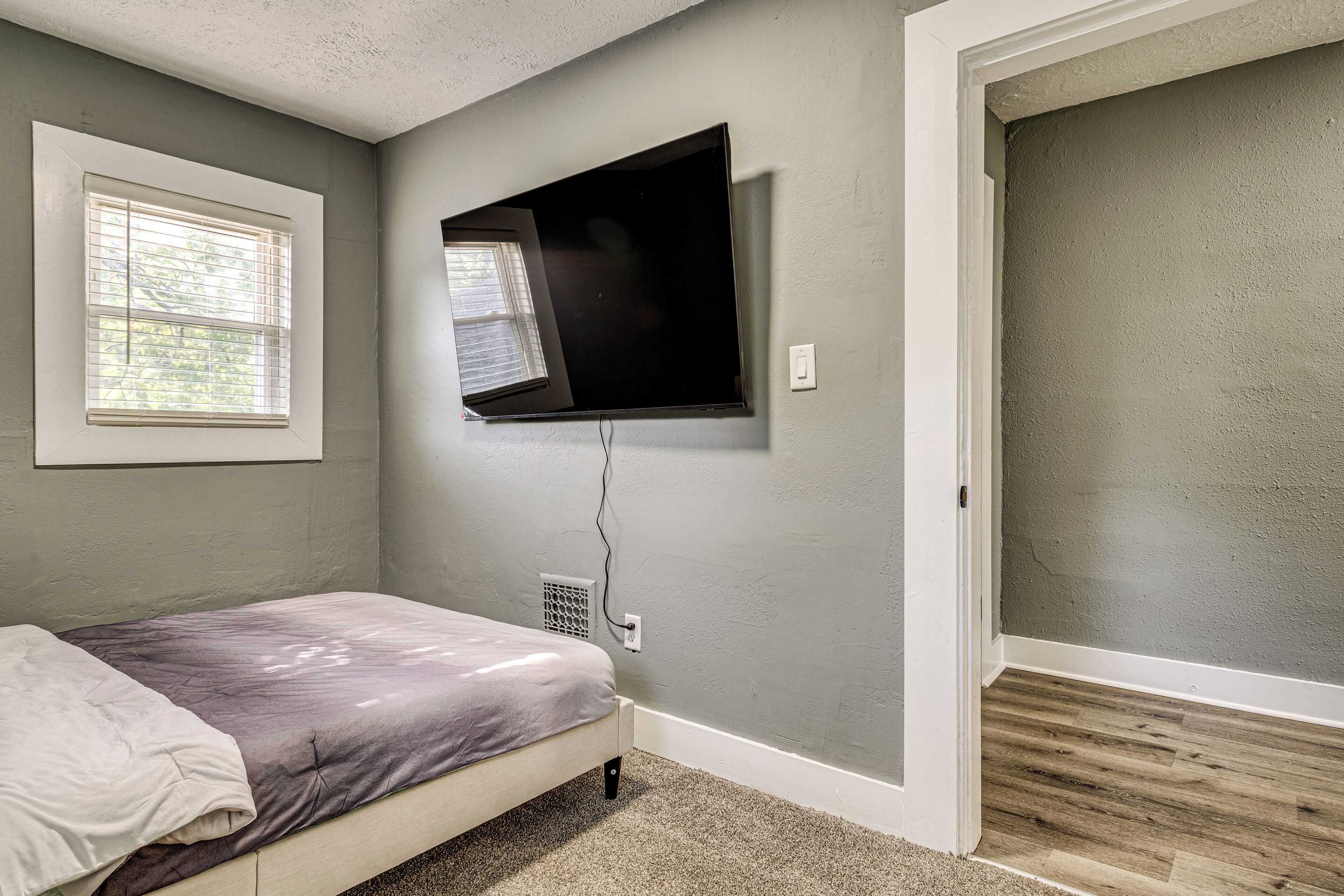 Une chambre à coucher avec un lit, un téléviseur fixé au mur, une fenêtre et une porte.