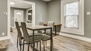 A dining area with a wooden table and chairs, a window with blinds, and a hallway leading to a kitchen. - Explore Downtown & Mass Ave! 3BR Indy Townhome (Indianapolis)