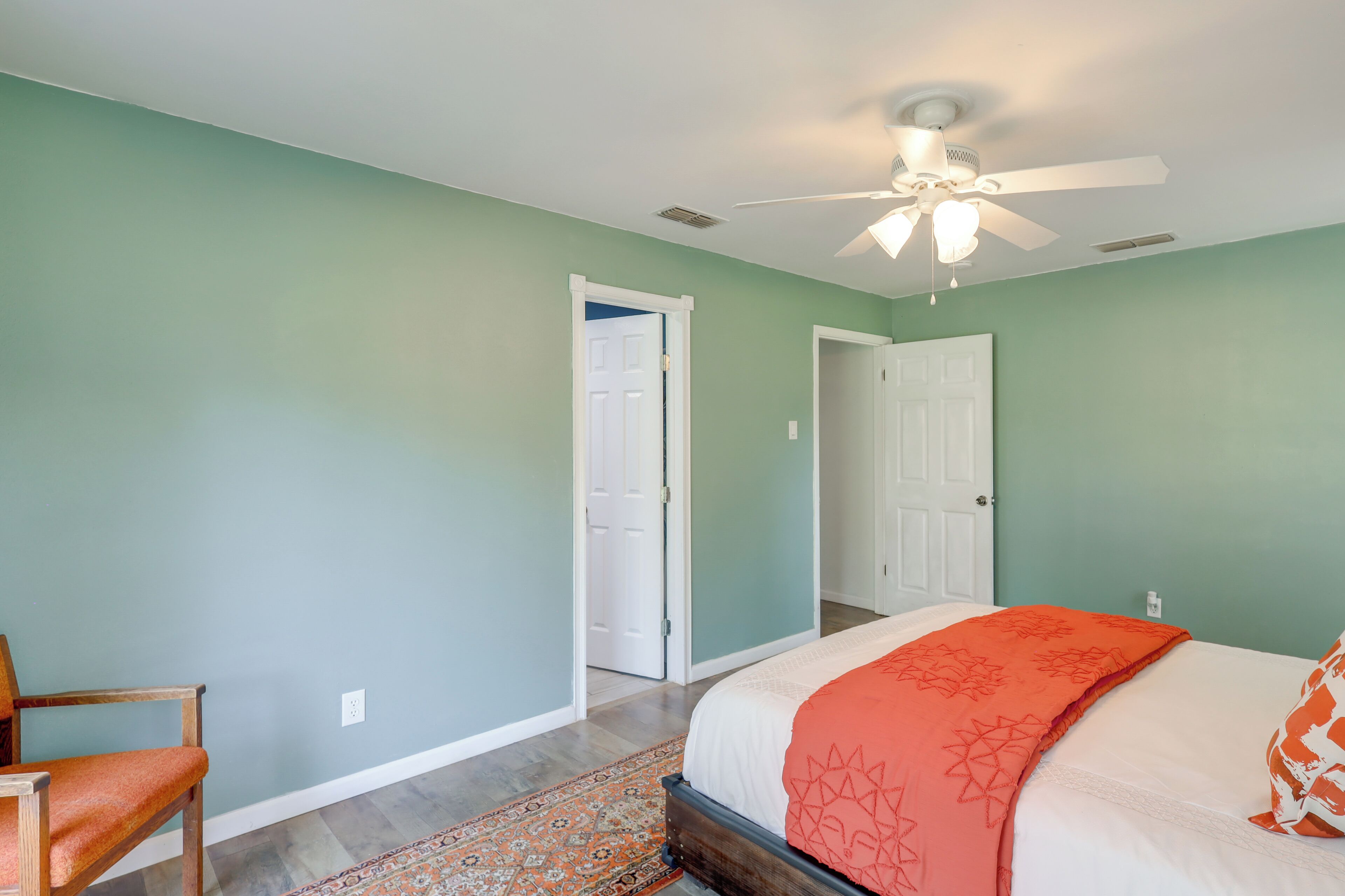 Une chambre à coucher avec un lit, une chaise, un ventilateur de plafond et une porte.