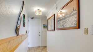 A hallway with a wooden baseboard, a door, and two wall-mounted light fixtures. - Resort Condo on Oahu: Ocean & Pool Views! (Hau`ula)