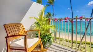 A wooden chair with a cushion, a potted plant, and a view of the ocean with palm trees. - Resort Condo on Oahu: Ocean & Pool Views! (Hau`ula)