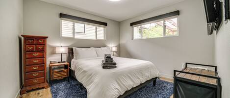 Een slaapkamer met een bed, een dressoir, een lamp en een raam.