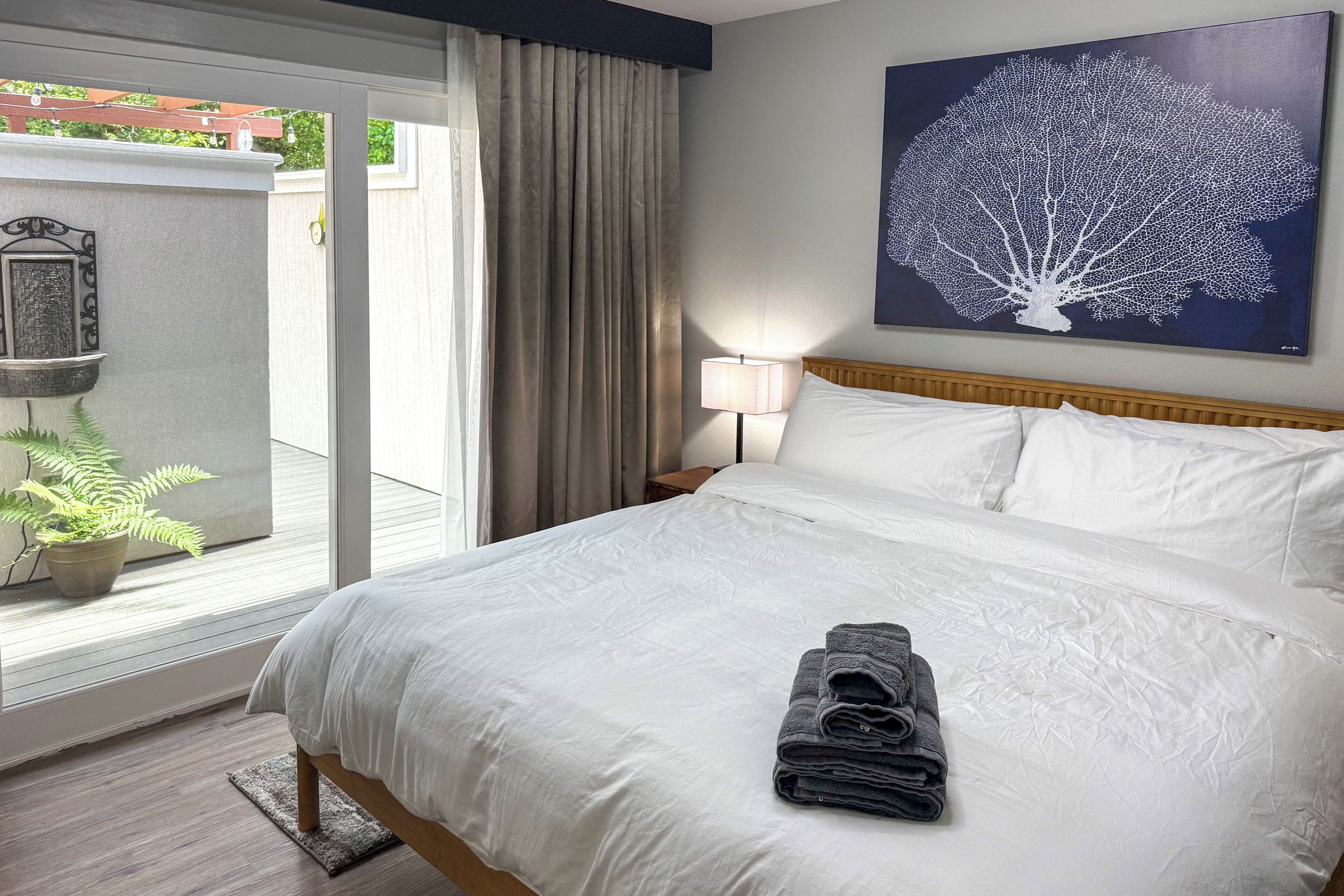 Ein Hotelzimmer mit einem großen Bett, Blick ins Freie, einem Bild an der Wand und einem Nachttisch mit Lampe.