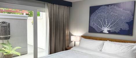 Ein Hotelzimmer mit einem großen Bett, Blick ins Freie, einem Bild an der Wand und einem Nachttisch mit Lampe.