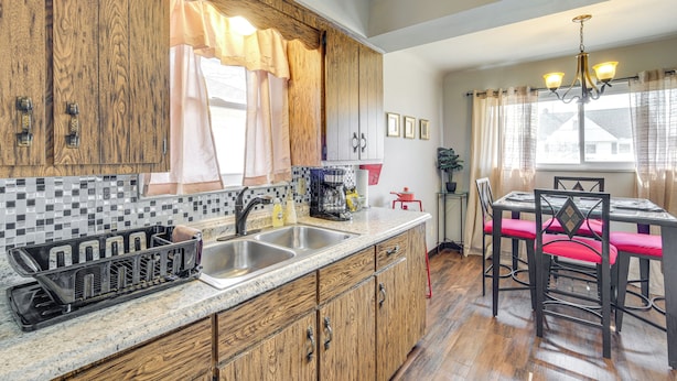 A kitchen with wooden cabinets, a granite countertop, a sink, and a dining area with a table and chairs. - 8 Mi to Dtwn Cleveland: Quiet Home w/ Fenced Yard (Garfield Heights)